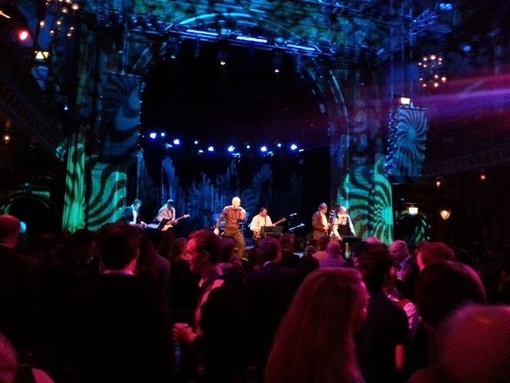 SMASH på scen i en festsalong med färgat scenljus och publik